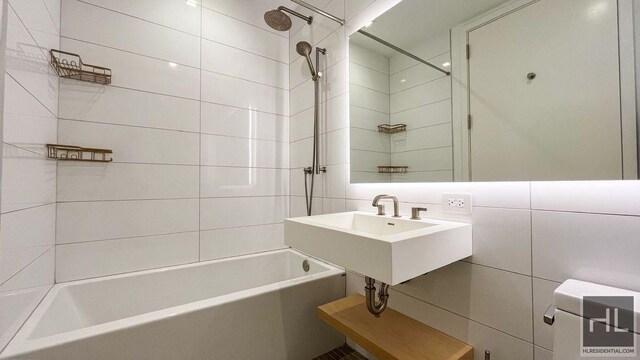 full bathroom with a sink, washtub / shower combination, and tile walls