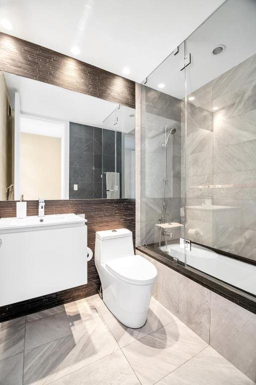 full bathroom with tile walls, combined bath / shower with glass door, vanity, and toilet