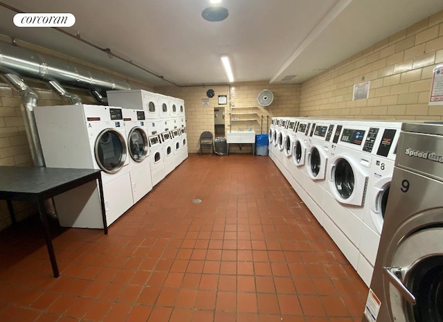 common laundry area with stacked washer and dryer, brick wall, dark tile patterned floors, and washing machine and clothes dryer