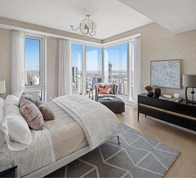 bedroom with wood finished floors, wallpapered walls, a view of city, and a chandelier