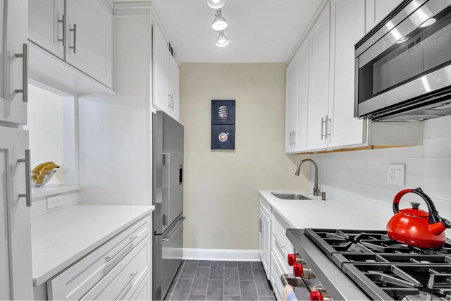 kitchen featuring appliances with stainless steel finishes, a sink, baseboards, white cabinets, and light countertops