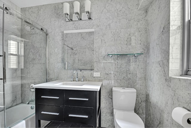 bathroom featuring toilet, shower / bath combination with glass door, vanity, and tile walls