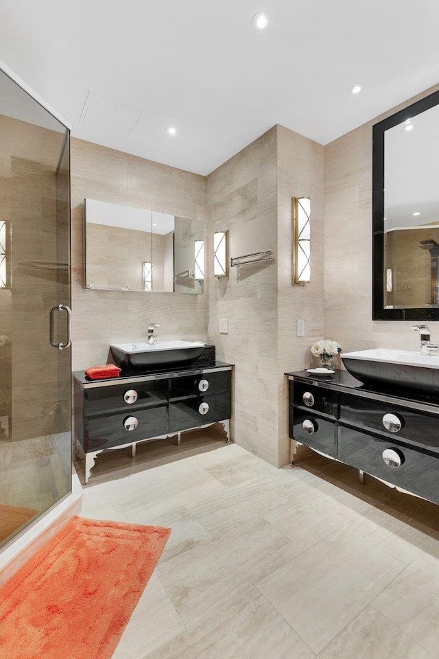 bathroom with a sink, a stall shower, two vanities, and tile walls