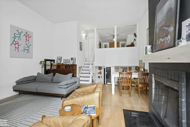 living room featuring light wood-style floors, a ceiling fan, a fireplace, and stairs