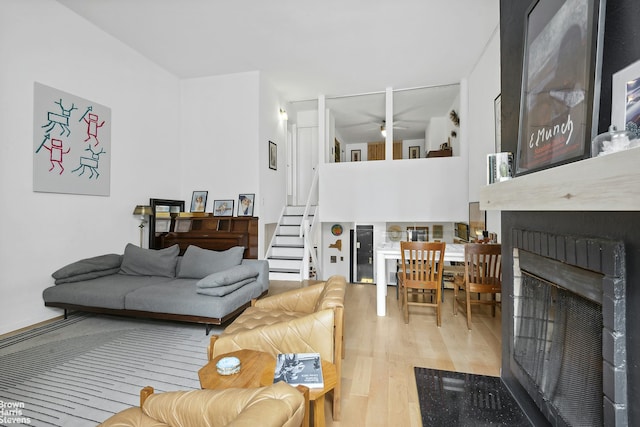 living area featuring a large fireplace, ceiling fan, stairway, and wood finished floors