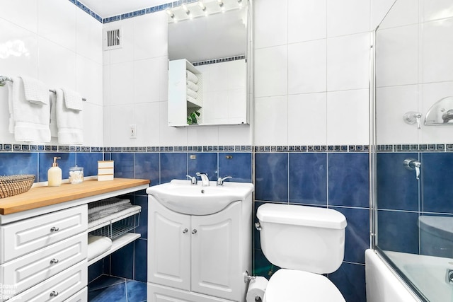 full bathroom featuring enclosed tub / shower combo, tile walls, toilet, and vanity