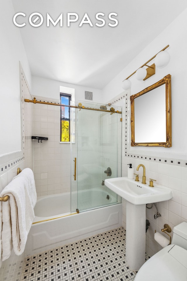 bathroom featuring visible vents, toilet, tile walls, and shower / bath combination with glass door