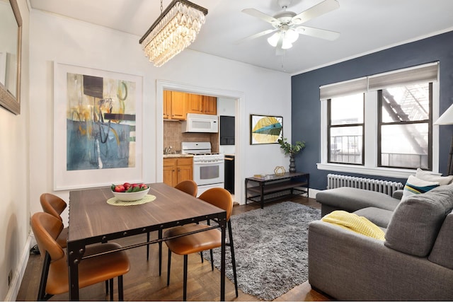 dining area featuring crown molding, wood finished floors, radiator heating unit, and ceiling fan with notable chandelier