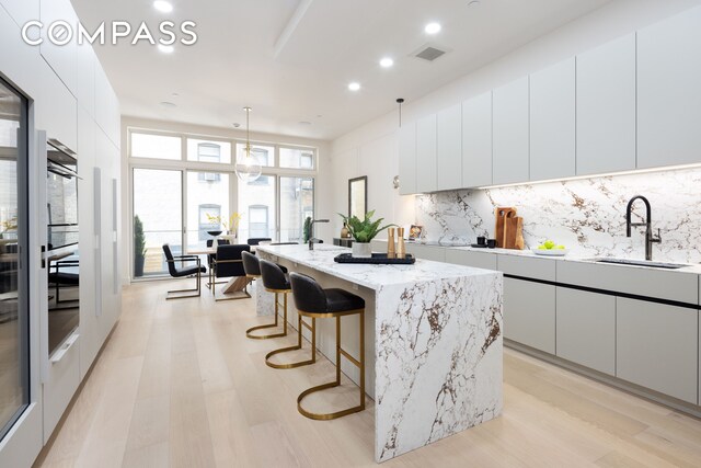 kitchen with sink, white cabinetry, decorative light fixtures, a center island with sink, and backsplash