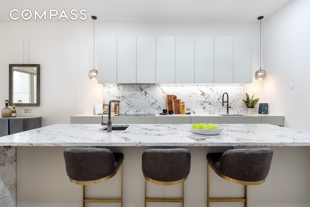 kitchen with decorative backsplash, white cabinets, a sink, and a kitchen breakfast bar