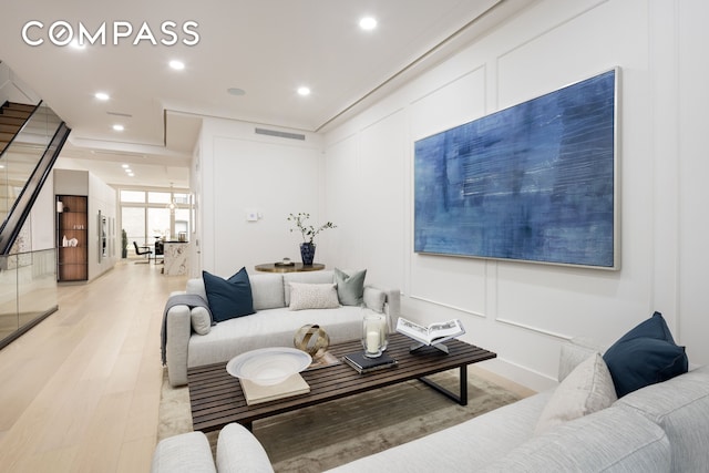 living area featuring light wood finished floors, visible vents, a decorative wall, and recessed lighting