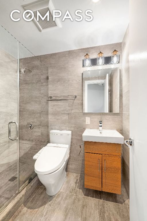 full bathroom featuring toilet, a shower stall, tile walls, and vanity