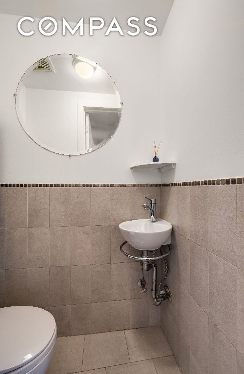 bathroom featuring tile walls, toilet, wainscoting, a sink, and tile patterned flooring