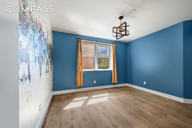 spare room featuring baseboards, wood finished floors, and an inviting chandelier