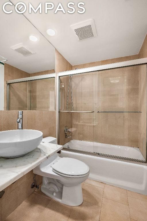 full bathroom featuring enclosed tub / shower combo, sink, tile walls, and toilet