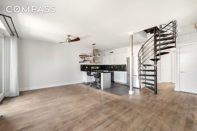 unfurnished living room featuring dark wood-style floors, stairway, a sink, ceiling fan, and baseboards