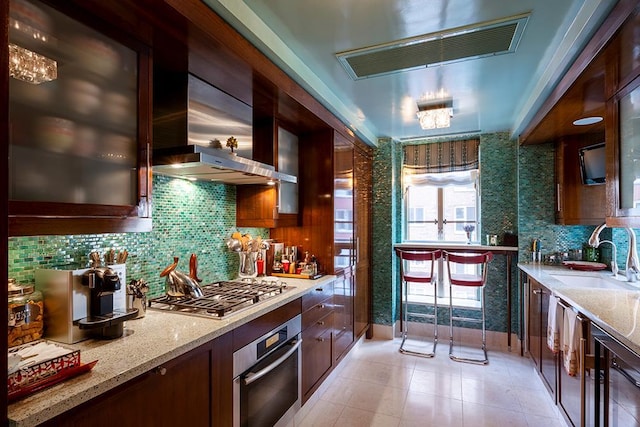 kitchen with range hood, light stone counters, a sink, stainless steel appliances, and glass insert cabinets