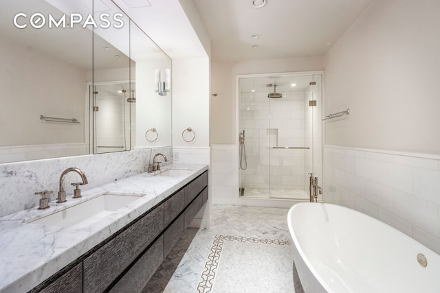 215 Sullivan St Unit Thc, New York City, NY 10012 - bathroom featuring a stall shower, a freestanding bath, double vanity, tile walls, and wainscoting
