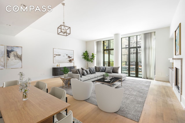 living room with a notable chandelier, light wood-style flooring, expansive windows, a glass covered fireplace, and baseboards