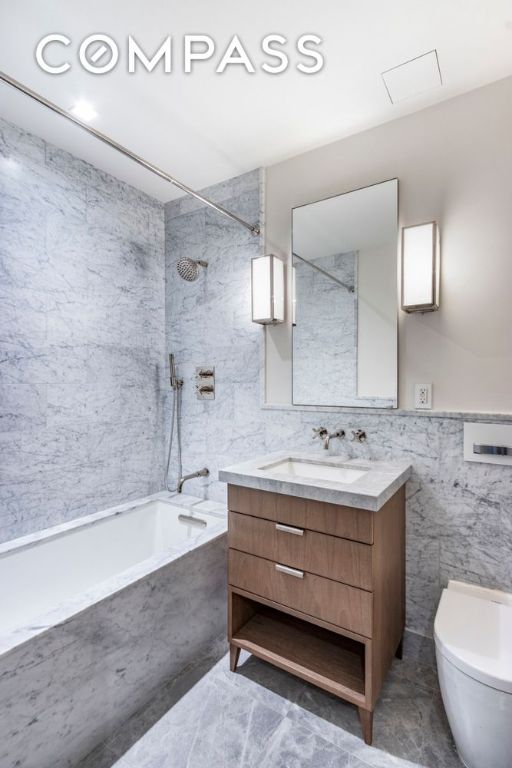 full bathroom featuring tiled shower / bath, vanity, toilet, and tile walls