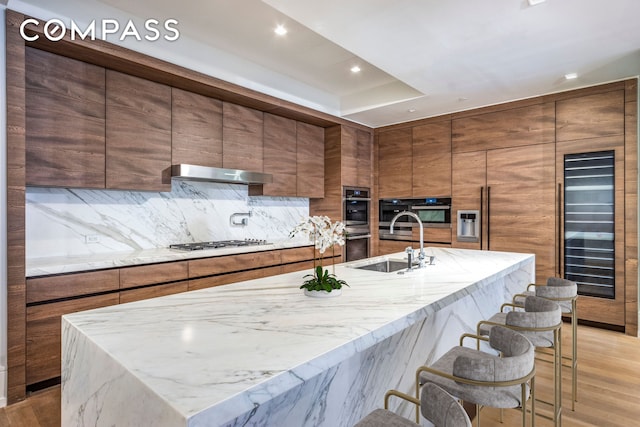 215 Sullivan St Unit Thc, New York City, NY 10012 - kitchen featuring beverage cooler, modern cabinets, under cabinet range hood, brown cabinetry, and recessed lighting