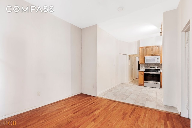 kitchen featuring stainless steel electric range oven, light brown cabinetry, light hardwood / wood-style flooring, and tasteful backsplash