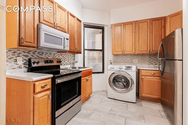 kitchen with a sink, tasteful backsplash, appliances with stainless steel finishes, light countertops, and washer / dryer