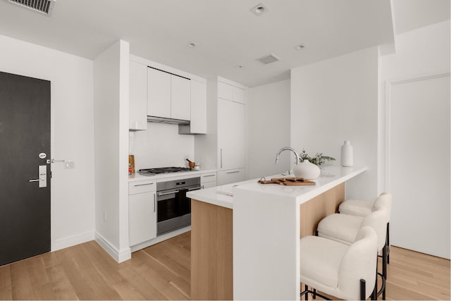 kitchen with visible vents, a breakfast bar, stainless steel appliances, light countertops, and white cabinetry