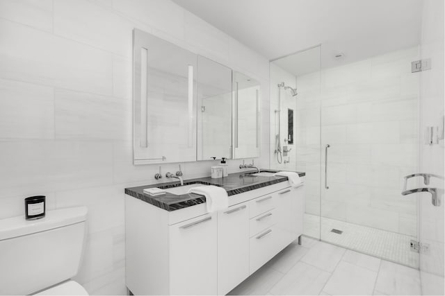 bathroom with double vanity, a stall shower, tile walls, toilet, and a sink