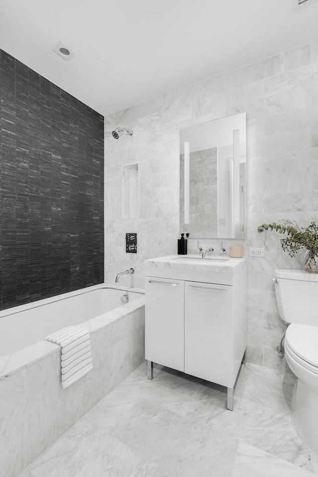 bathroom featuring marble finish floor, tiled shower / bath, tile walls, toilet, and vanity