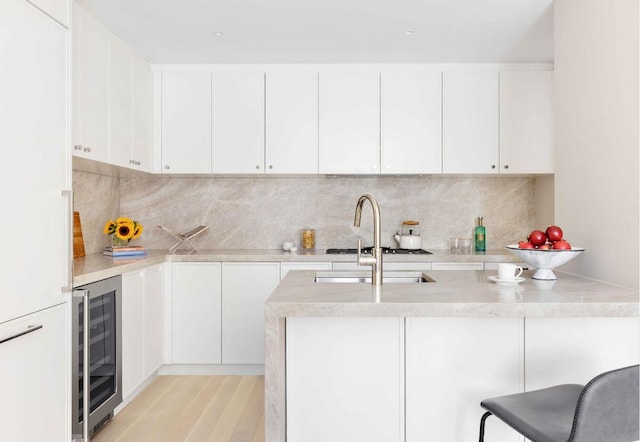 kitchen with a breakfast bar, wine cooler, light hardwood / wood-style floors, tasteful backsplash, and white cabinets