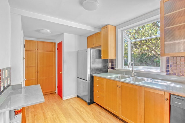 kitchen featuring a sink, black dishwasher, light countertops, freestanding refrigerator, and glass insert cabinets