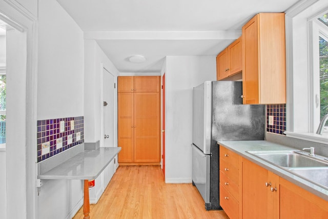 kitchen with light countertops, light wood finished floors, a sink, and freestanding refrigerator