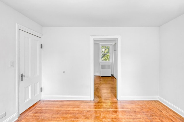 empty room featuring light wood-type flooring, radiator, and baseboards