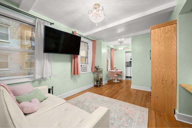 living area featuring cooling unit, light wood-style flooring, baseboards, and an inviting chandelier