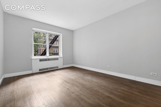 empty room with radiator heating unit, dark wood finished floors, and baseboards