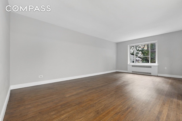 empty room featuring radiator heating unit, dark wood-style flooring, and baseboards