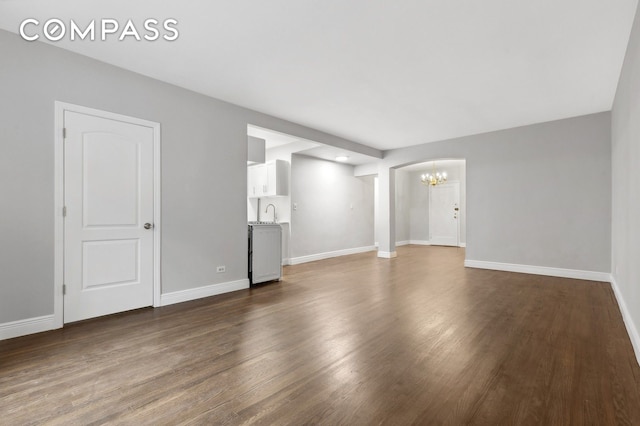 unfurnished living room featuring a chandelier, dark wood-type flooring, and baseboards