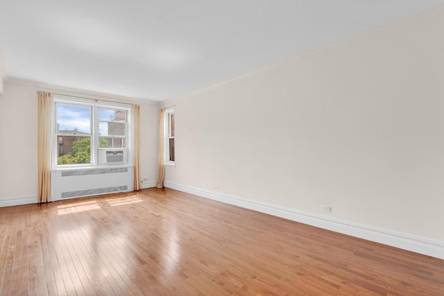 empty room featuring radiator heating unit, light wood-type flooring, crown molding, and cooling unit