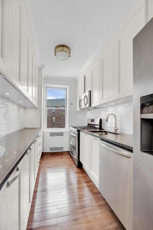 kitchen with white cabinetry, stainless steel appliances, sink, and radiator heating unit