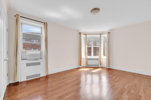 empty room with wood finished floors, radiator, a healthy amount of sunlight, and baseboards