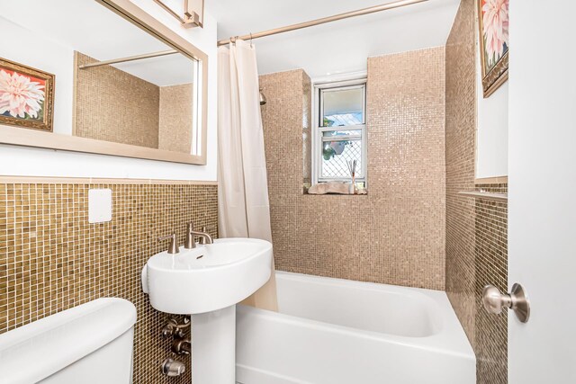 bathroom with toilet, a wainscoted wall, tile walls, and shower / tub combo with curtain