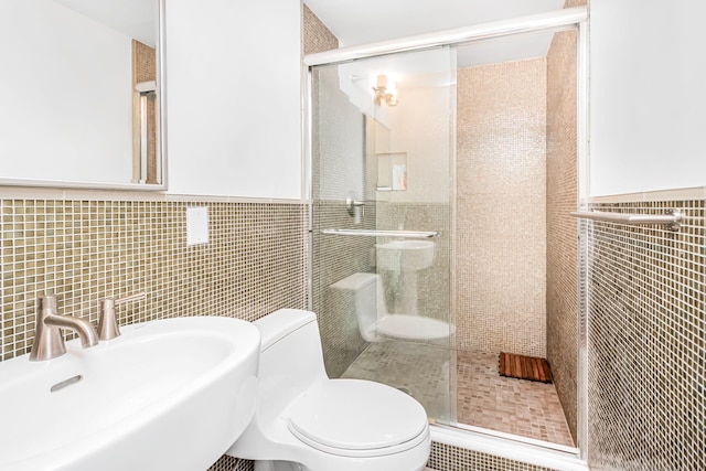 bathroom with tile walls, a sink, toilet, and a shower stall