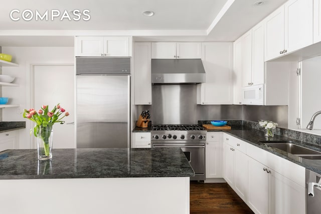 kitchen featuring under cabinet range hood, high quality appliances, dark stone counters, white cabinets, and a sink