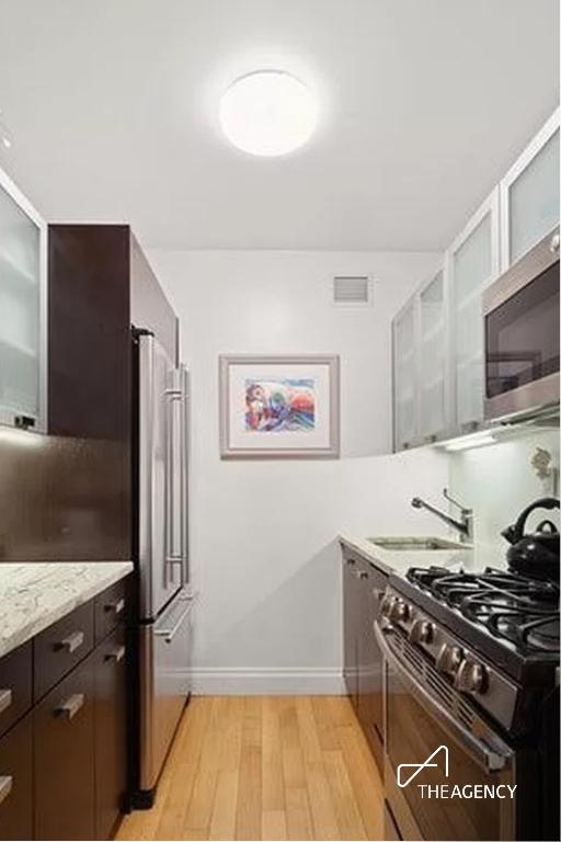 kitchen with sink, dark brown cabinets, stainless steel appliances, light stone countertops, and light wood-type flooring