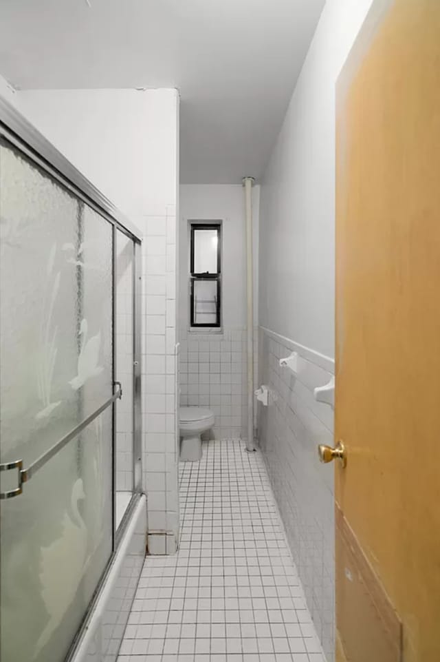 full bath featuring toilet, tile patterned floors, shower / bath combination with glass door, tile walls, and a wainscoted wall