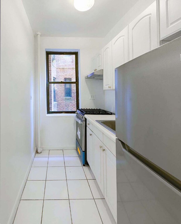 kitchen with appliances with stainless steel finishes, sink, light tile patterned floors, and white cabinets