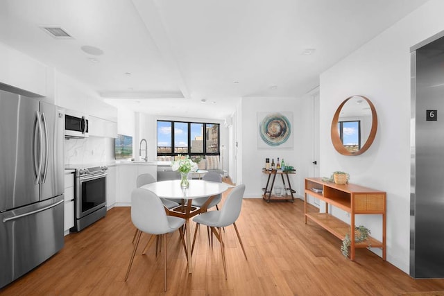 dining space featuring light wood-style floors, visible vents, and baseboards