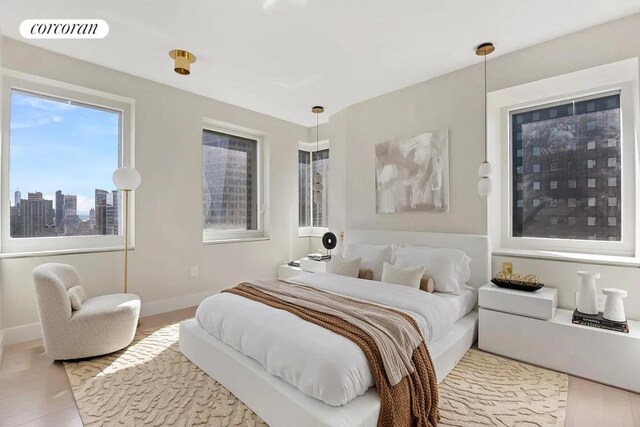 bedroom with baseboards, wood finished floors, visible vents, and a city view