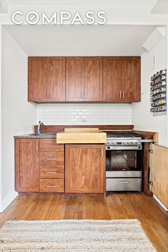 kitchen featuring stainless steel range with gas cooktop, brown cabinets, decorative backsplash, a sink, and hardwood / wood-style floors